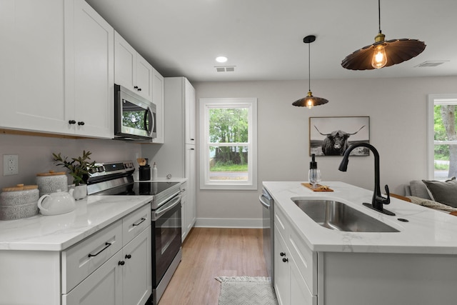 kitchen with appliances with stainless steel finishes, a sink, baseboards, light wood-style flooring, and white cabinets