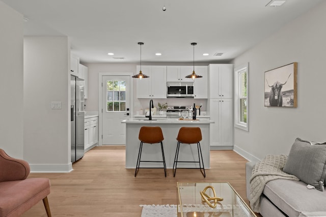 kitchen featuring stainless steel appliances, light countertops, white cabinetry, a kitchen bar, and an island with sink