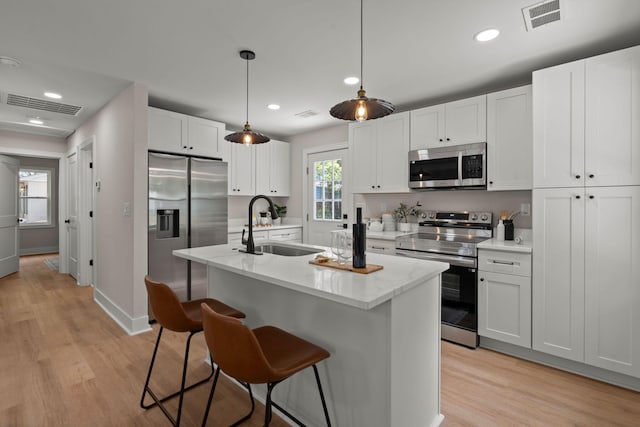 kitchen with appliances with stainless steel finishes, a sink, a breakfast bar, white cabinetry, and light wood-style flooring