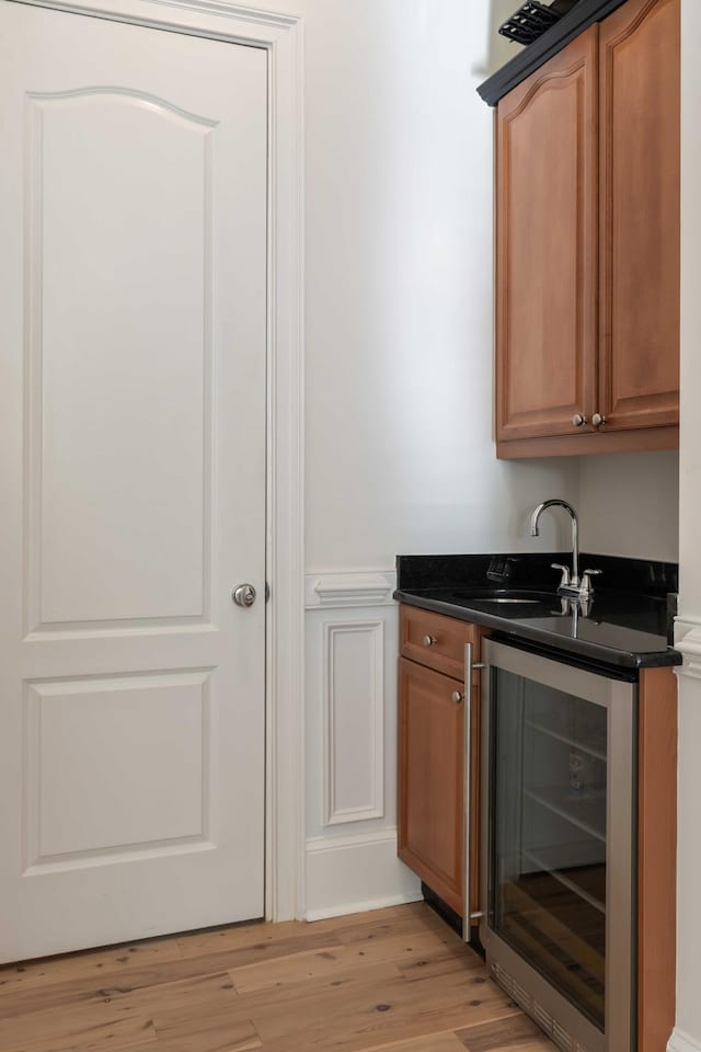 bar featuring light wood-style flooring, beverage cooler, a sink, a decorative wall, and a wainscoted wall