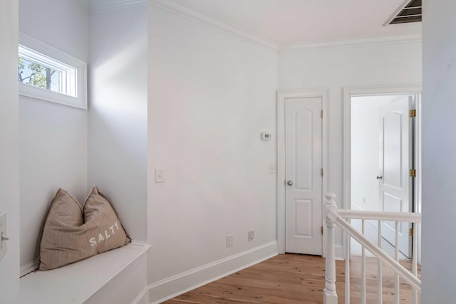 hallway featuring baseboards, light wood-style floors, visible vents, and crown molding