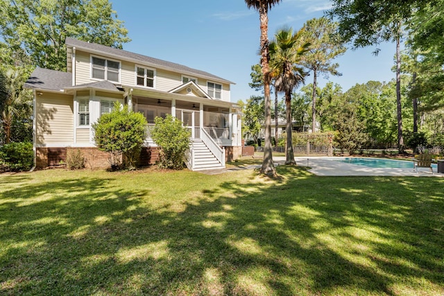 back of property with a yard, an outdoor pool, stairway, and a sunroom