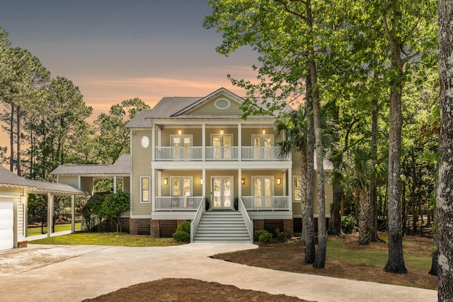 neoclassical / greek revival house with french doors, concrete driveway, a balcony, a porch, and stairs
