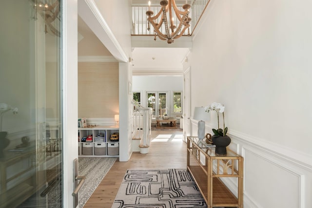 entryway featuring wood finished floors, french doors, a high ceiling, a notable chandelier, and ornamental molding