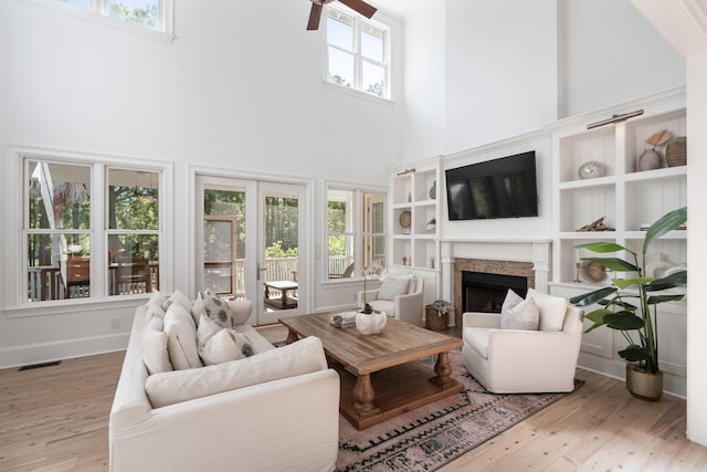 living area featuring a healthy amount of sunlight, a fireplace, a towering ceiling, and wood finished floors
