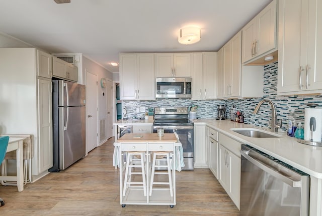 kitchen with a sink, light countertops, appliances with stainless steel finishes, light wood-type flooring, and decorative backsplash