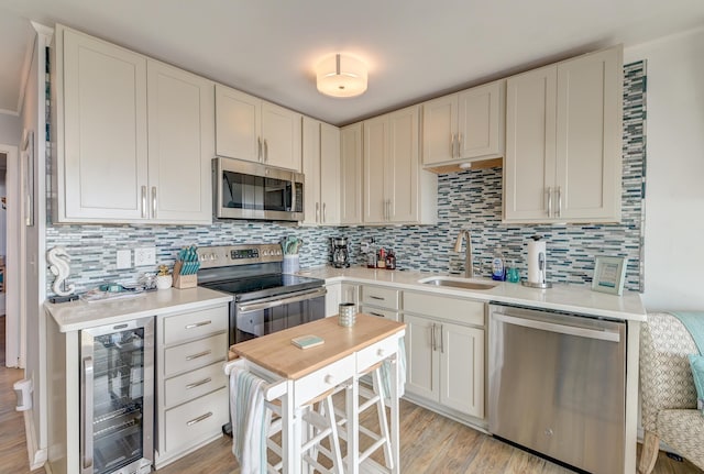 kitchen featuring tasteful backsplash, light countertops, appliances with stainless steel finishes, a sink, and beverage cooler