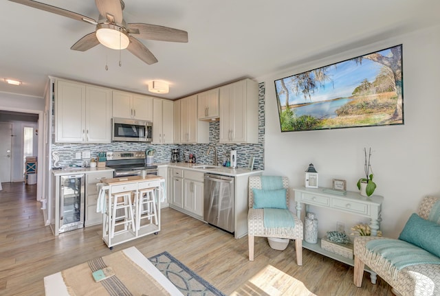 kitchen with appliances with stainless steel finishes, beverage cooler, light wood-style floors, and tasteful backsplash