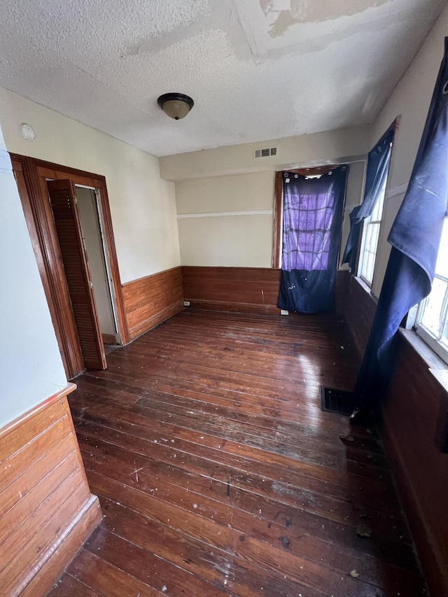 empty room featuring dark hardwood / wood-style flooring, a textured ceiling, and wooden walls