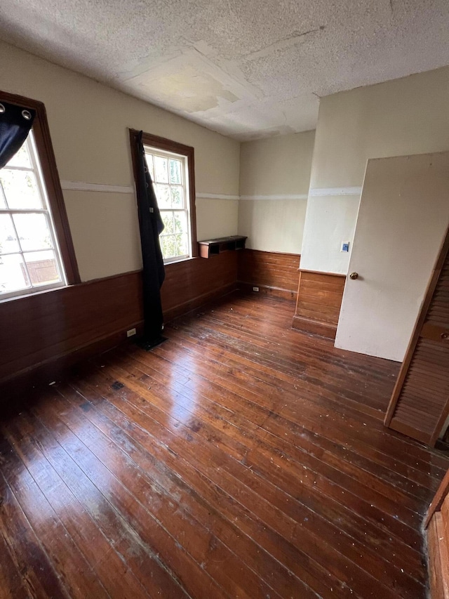 unfurnished room with a textured ceiling, dark wood-type flooring, and wood walls