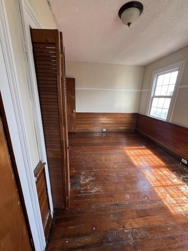 unfurnished room featuring a textured ceiling, wooden walls, and dark hardwood / wood-style floors