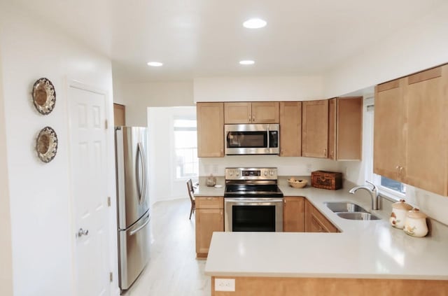 kitchen featuring stainless steel appliances, recessed lighting, light countertops, a sink, and a peninsula