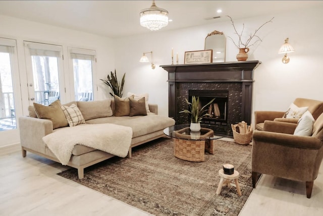 living room featuring light wood finished floors, a premium fireplace, and a notable chandelier