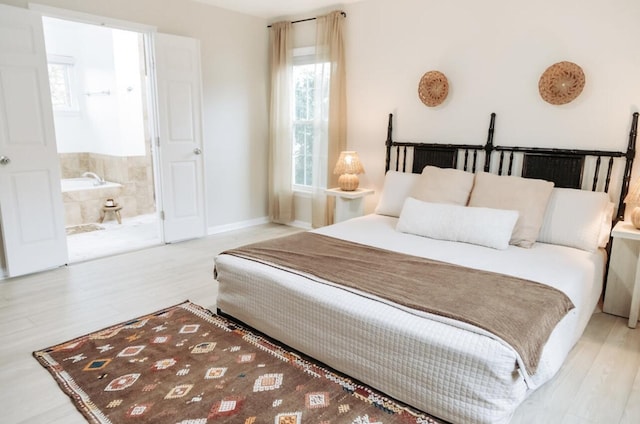 bedroom with ensuite bath, light wood-style flooring, and baseboards