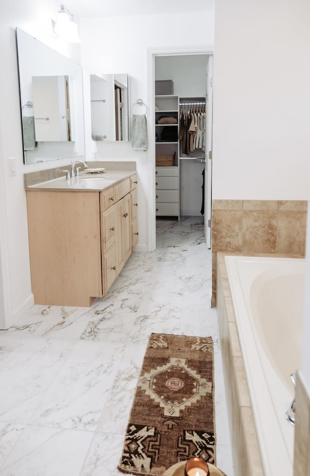 full bath featuring marble finish floor, vanity, a walk in closet, and a bath