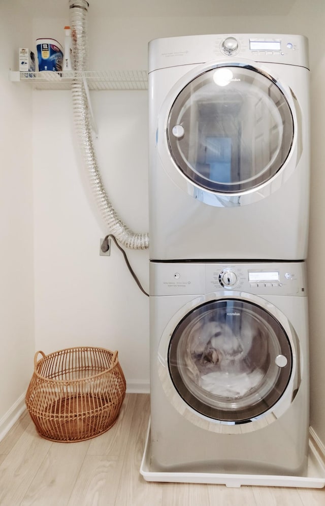 laundry room with stacked washer / dryer, laundry area, baseboards, and wood finished floors