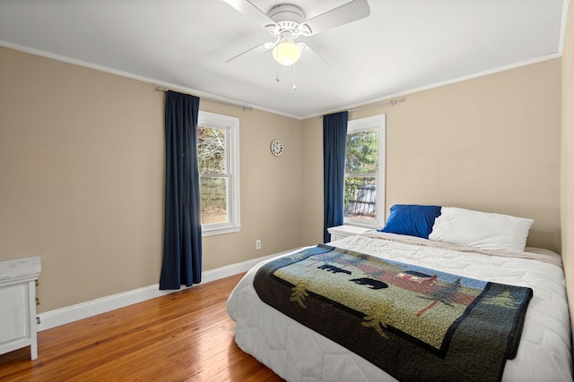 bedroom with ceiling fan, wood-type flooring, ornamental molding, and multiple windows