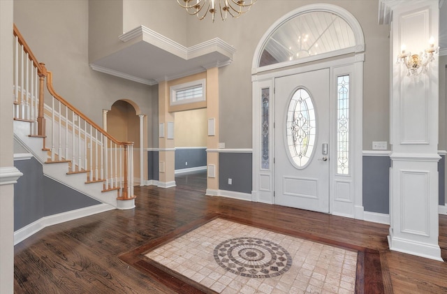 foyer entrance featuring a towering ceiling, decorative columns, hardwood / wood-style flooring, ornamental molding, and an inviting chandelier