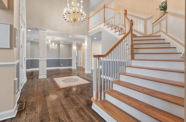 entryway featuring ornate columns, ornamental molding, dark hardwood / wood-style flooring, a notable chandelier, and a towering ceiling