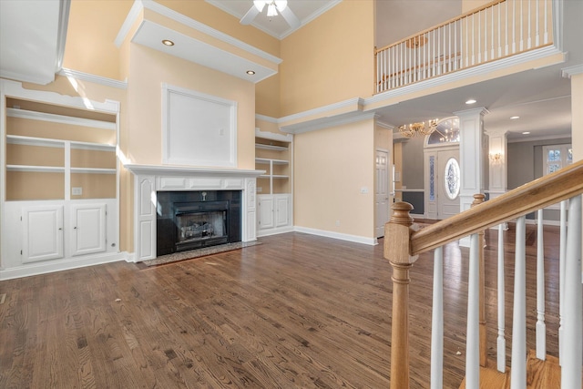 unfurnished living room with a towering ceiling, built in features, a fireplace, ornamental molding, and dark wood-type flooring