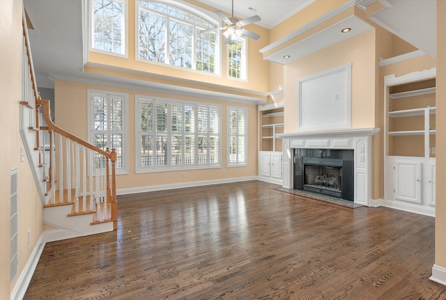 unfurnished living room featuring ceiling fan, dark hardwood / wood-style floors, a fireplace, ornamental molding, and built in shelves