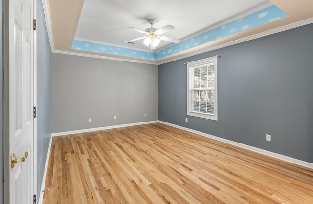 empty room with ornamental molding, a raised ceiling, ceiling fan, and light wood-type flooring