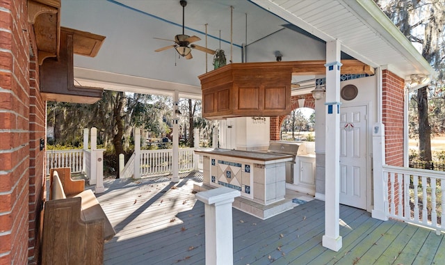 wooden deck with grilling area, an outdoor kitchen, ceiling fan, and exterior bar