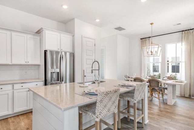 kitchen featuring stainless steel fridge, light hardwood / wood-style floors, white cabinetry, and a kitchen island with sink