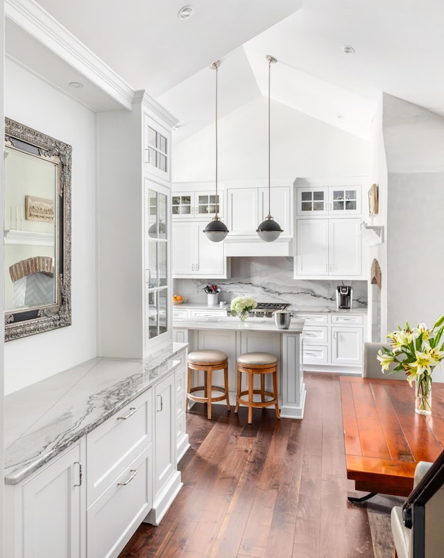 kitchen featuring pendant lighting, lofted ceiling, backsplash, white cabinets, and dark hardwood / wood-style flooring