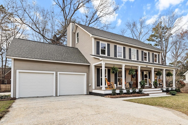 colonial home with covered porch, an attached garage, concrete driveway, and a shingled roof