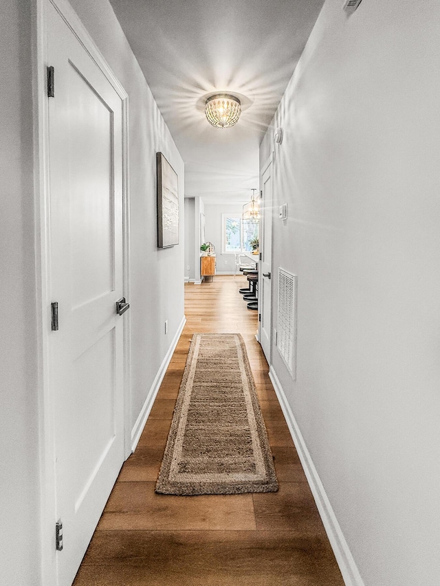 hallway with wood finished floors, visible vents, and baseboards