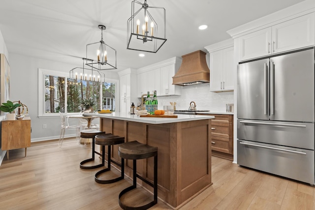 kitchen featuring premium range hood, light countertops, decorative backsplash, high quality fridge, and an inviting chandelier