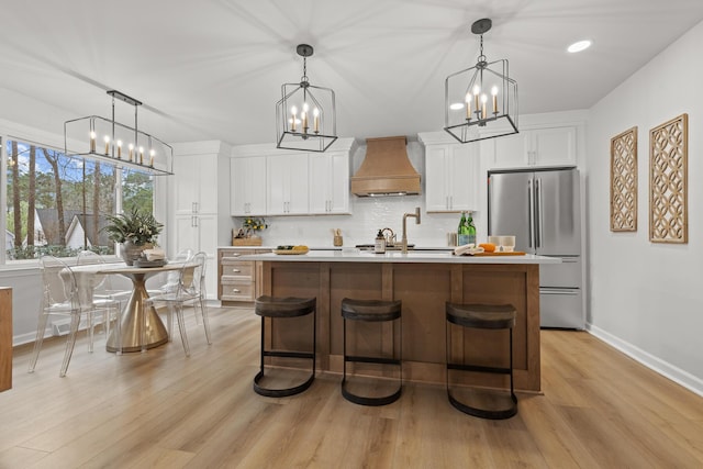 kitchen featuring premium range hood, backsplash, a notable chandelier, and freestanding refrigerator