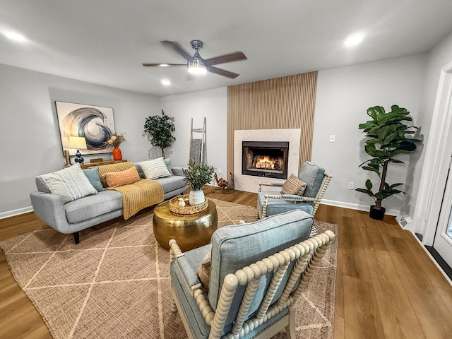 living room featuring a ceiling fan, wood finished floors, baseboards, and a large fireplace