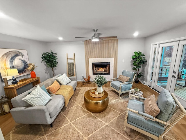 living room featuring a warm lit fireplace, wood finished floors, recessed lighting, baseboards, and ceiling fan