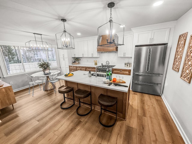 kitchen with a breakfast bar area, light countertops, white cabinets, high quality fridge, and backsplash