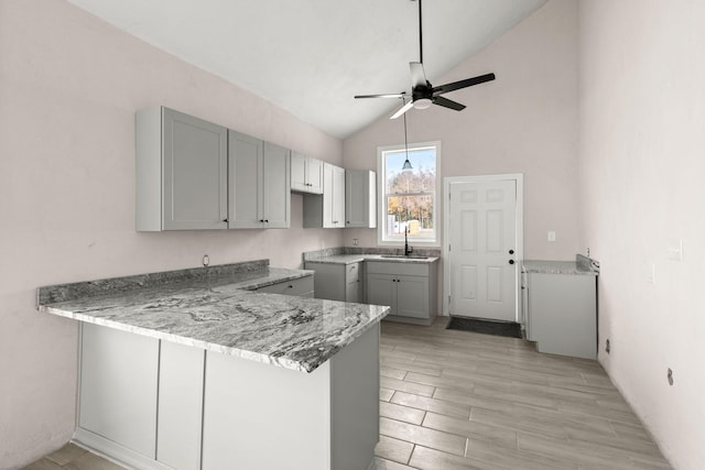 kitchen featuring kitchen peninsula, gray cabinets, vaulted ceiling, and sink