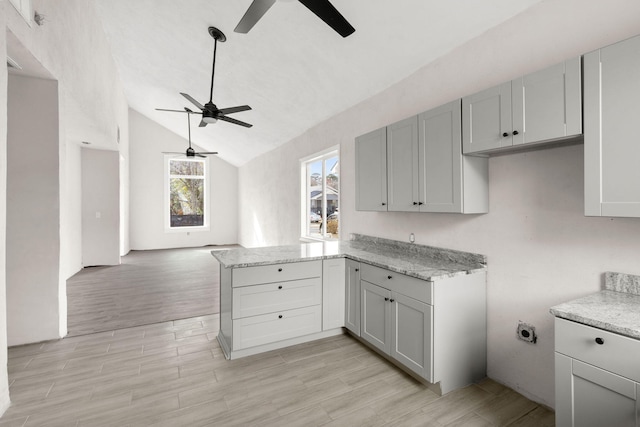 kitchen with kitchen peninsula, ceiling fan, light stone countertops, and vaulted ceiling