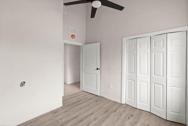 unfurnished bedroom featuring a high ceiling, a closet, light hardwood / wood-style flooring, and ceiling fan