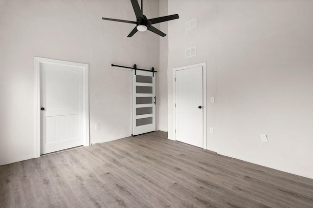 unfurnished bedroom featuring a towering ceiling, a barn door, light hardwood / wood-style flooring, and ceiling fan