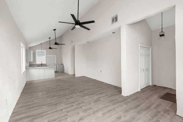 unfurnished living room with ceiling fan, light hardwood / wood-style floors, sink, and high vaulted ceiling