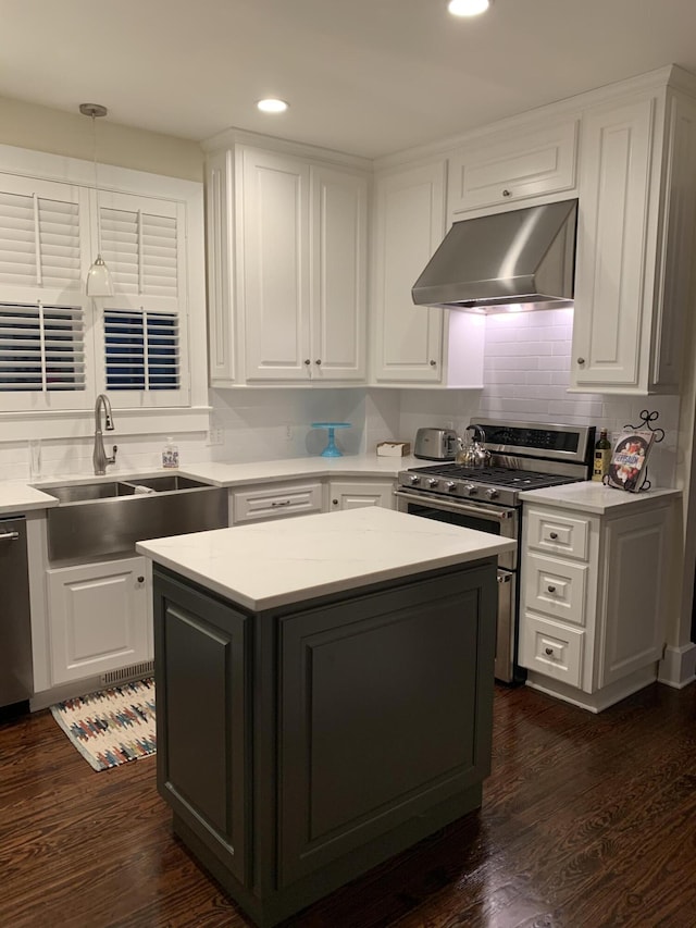 kitchen with pendant lighting, sink, dark wood-type flooring, extractor fan, and appliances with stainless steel finishes