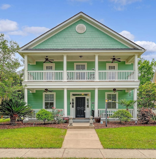 view of front of home with a ceiling fan, covered porch, a balcony, and a front lawn
