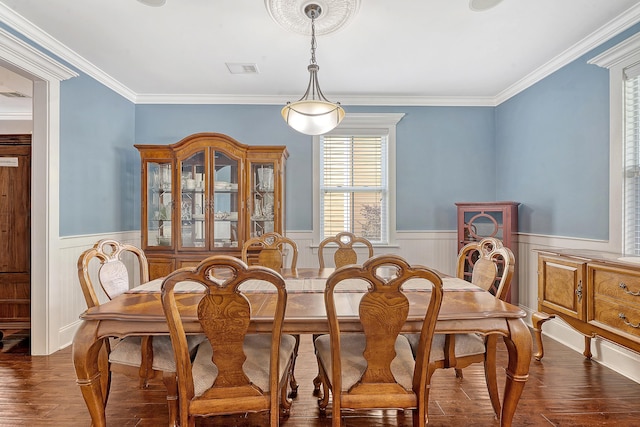 dining room with wood finished floors, a wainscoted wall, and crown molding