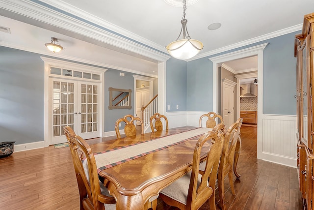 dining room featuring french doors, wainscoting, wood-type flooring, crown molding, and stairway