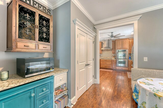 bar area with stainless steel appliances, wall chimney range hood, ceiling fan, hardwood / wood-style flooring, and decorative backsplash