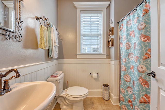 full bathroom featuring a sink, wainscoting, tile patterned floors, toilet, and curtained shower