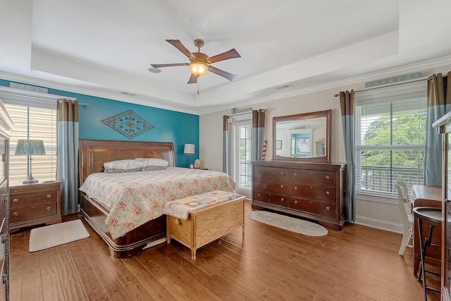 bedroom with a tray ceiling, wood finished floors, baseboards, a ceiling fan, and ornamental molding