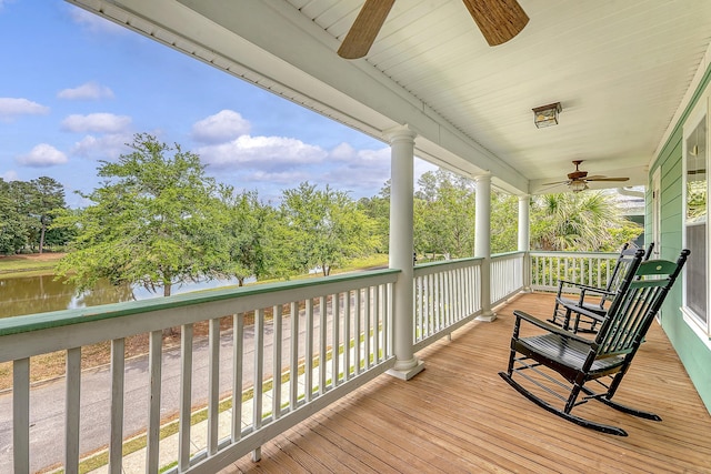 wooden terrace with a ceiling fan, a water view, and view of wooded area