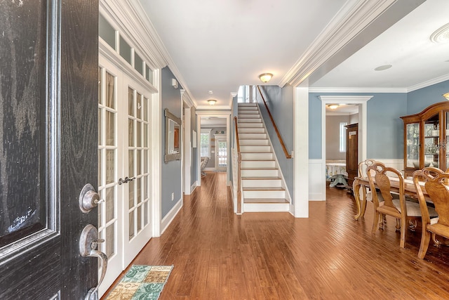 foyer entrance featuring stairway, french doors, wainscoting, wood finished floors, and crown molding
